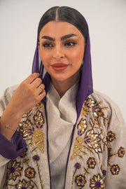 Woman wearing a beige open-front bisht abaya with gold and purple floral beadwork, purple chiffon lining, and relaxed fit.