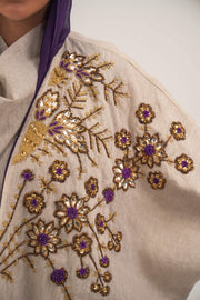 Woman wearing a beige open-front bisht abaya with gold and purple floral beadwork, purple chiffon lining, and relaxed fit.