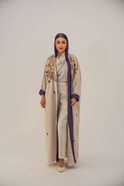 Woman wearing a beige open-front bisht abaya with gold and purple floral beadwork, purple chiffon lining, and relaxed fit.