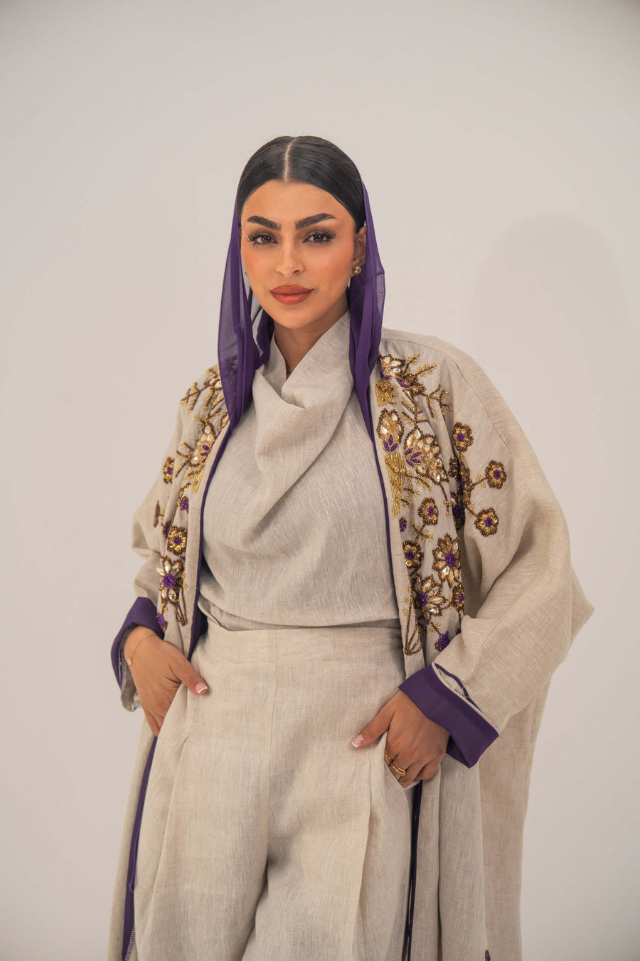 Woman wearing a lightweight linen open-front bisht abaya with gold and purple floral beadwork and purple chiffon lining.