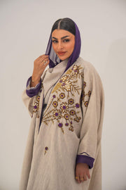 Woman wearing a beige open-front bisht abaya with gold and purple floral beadwork, purple chiffon lining, and relaxed fit.