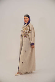 Woman wearing a beige open-front bisht abaya with gold and purple floral beadwork, purple chiffon lining, and relaxed fit.