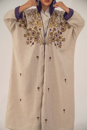 Woman wearing a beige open-front bisht abaya with gold and purple floral beadwork, purple chiffon lining, and relaxed fit.