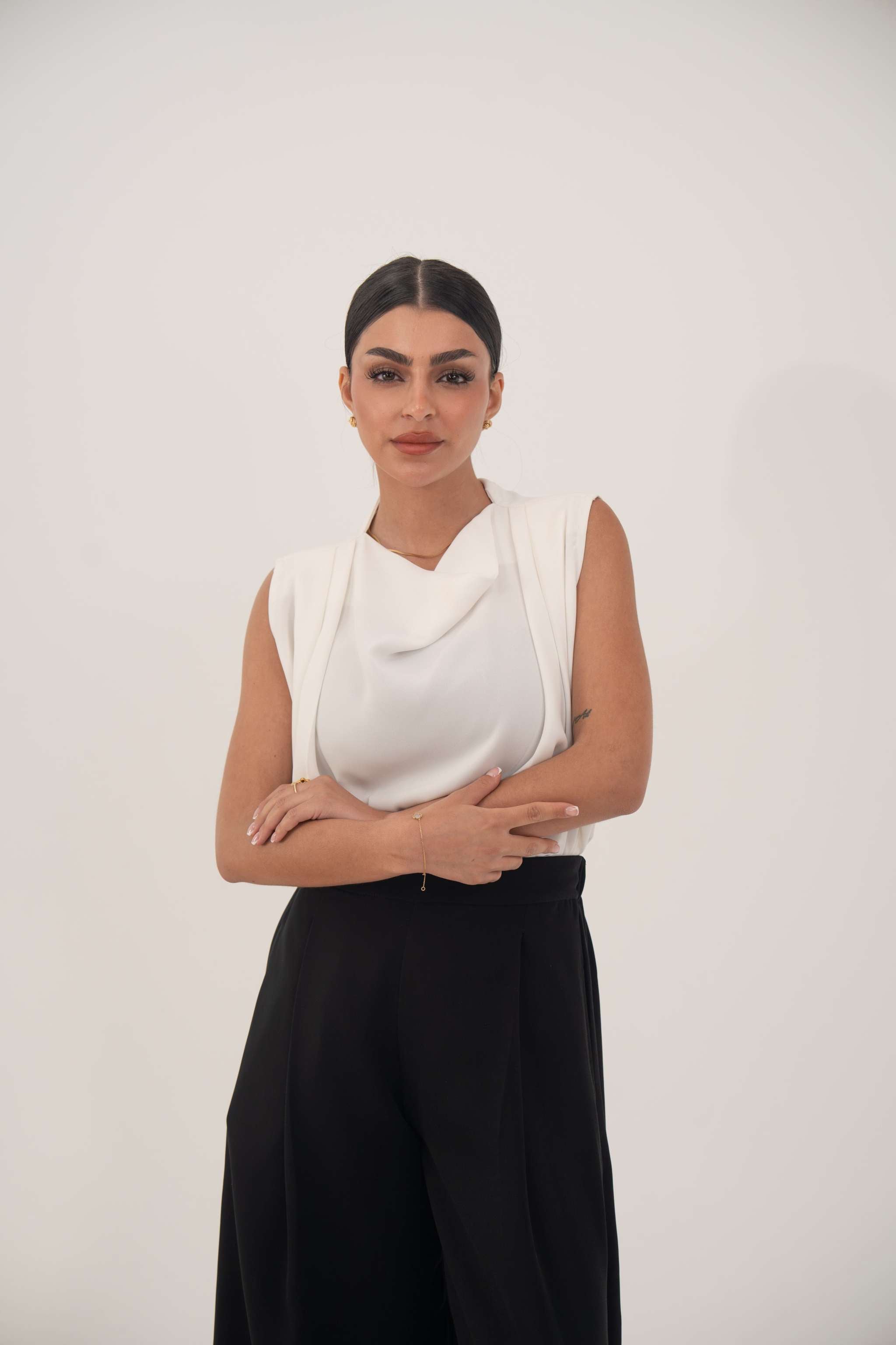 woman wearing sleeveless white silk top and black pants standing with arms crossed