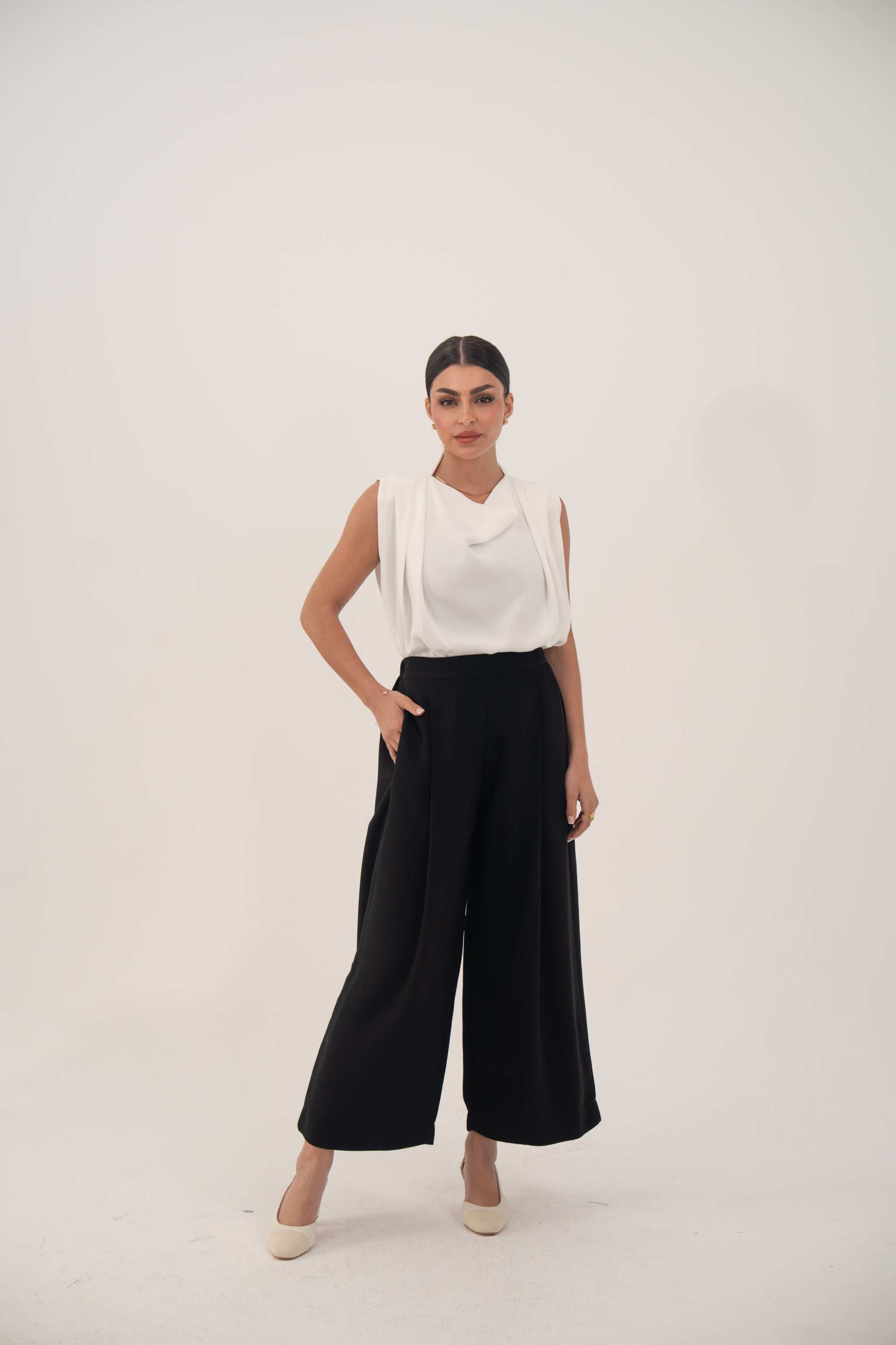 woman wearing wide-leg black silk pants and sleeveless white top in studio