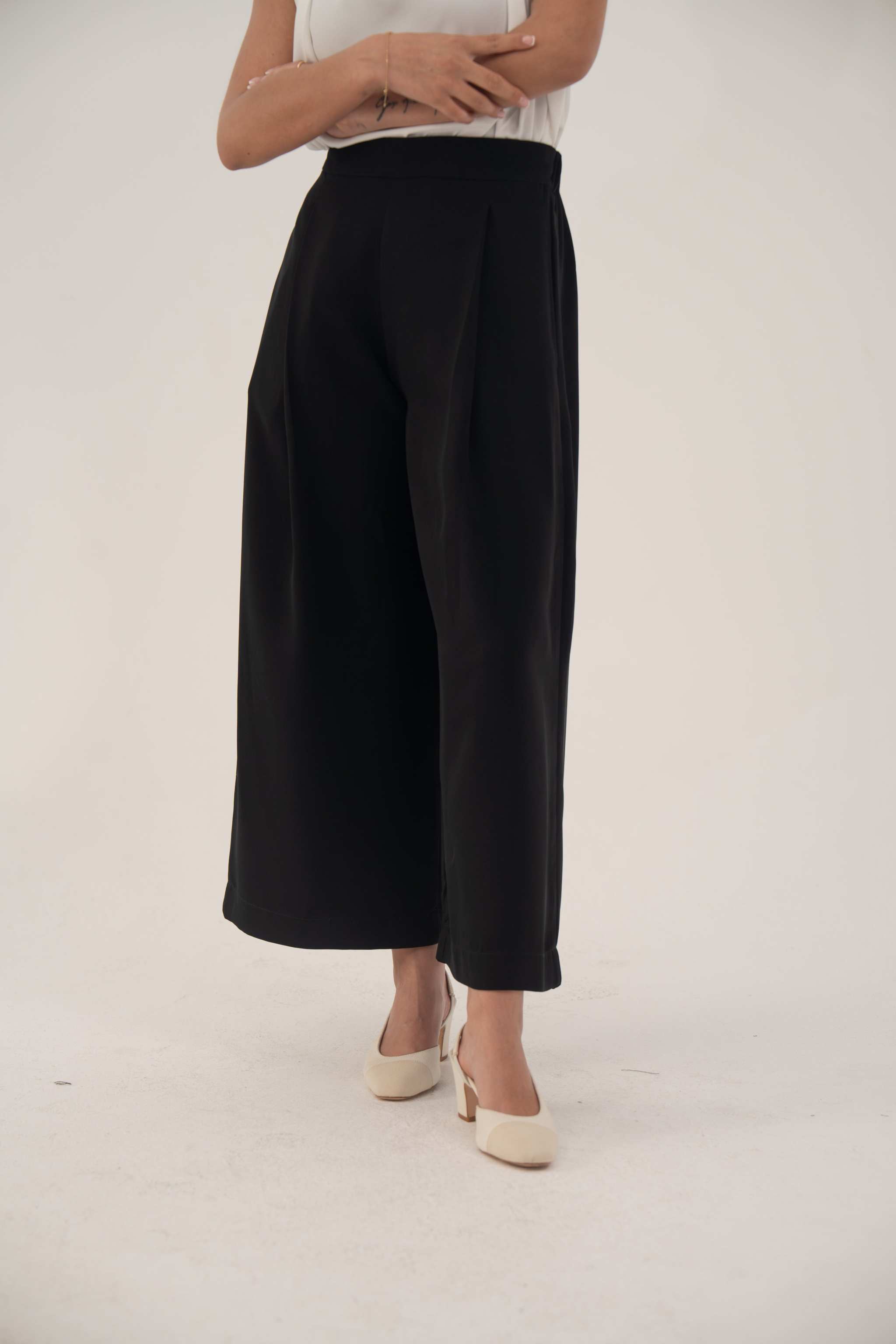 Wide-leg black pants with high waist and pleats, styled with white heels