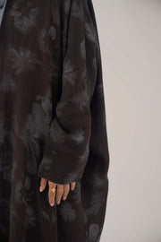 Dark silk abaya with subtle floral pattern, wide cut, open front, soft lapel, and long sleeves.