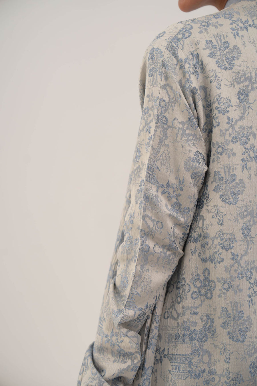 close-up of jacquard silk abaya with soft blue floral pattern on light fabric, featuring long sleeves and elegant texture