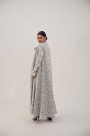 Woman wearing a long open-front jacquard silk abaya with a soft elegant pattern and simple lapel, styled with heels.