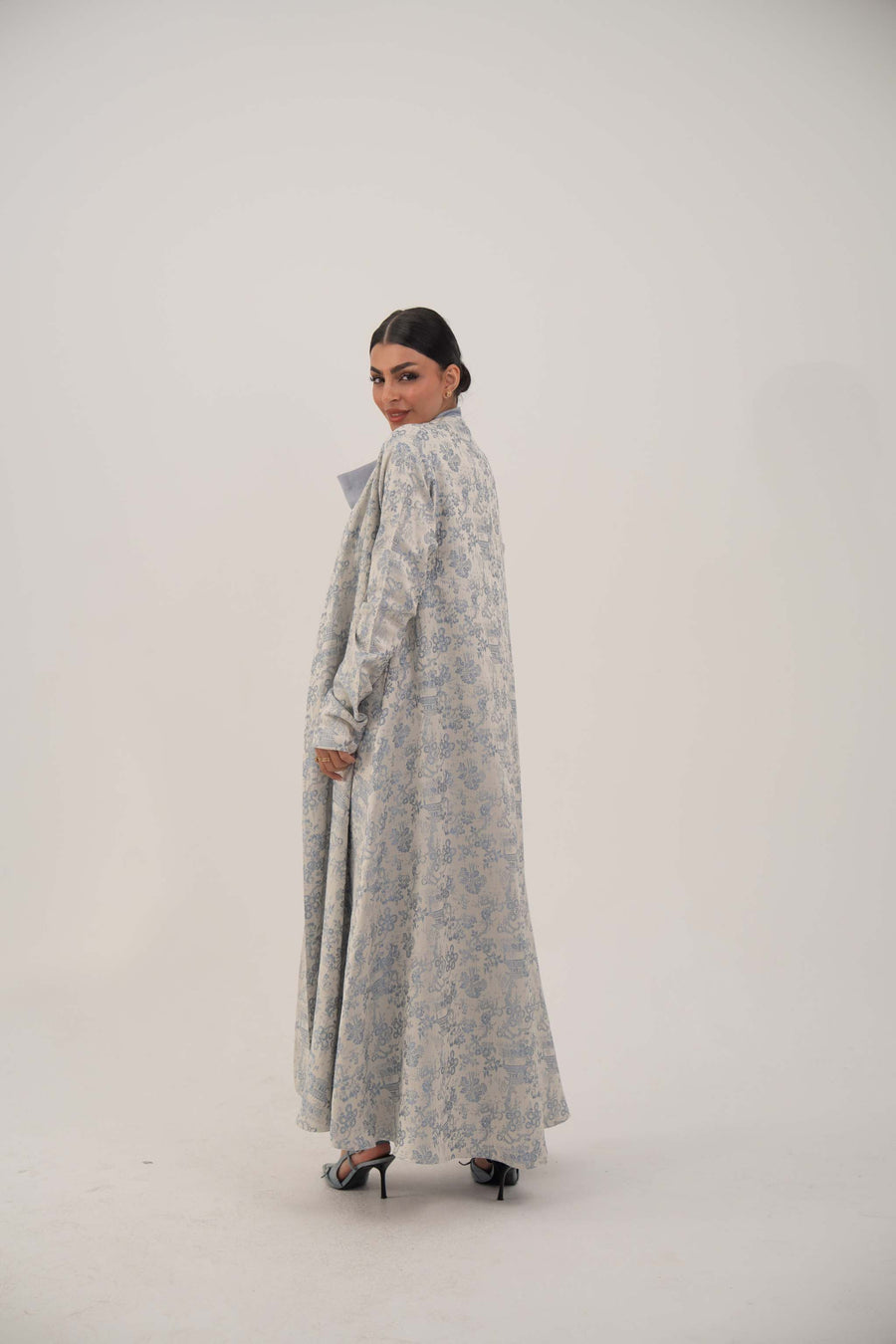Woman wearing a long open-front jacquard silk abaya with a soft elegant pattern and simple lapel, styled with heels.