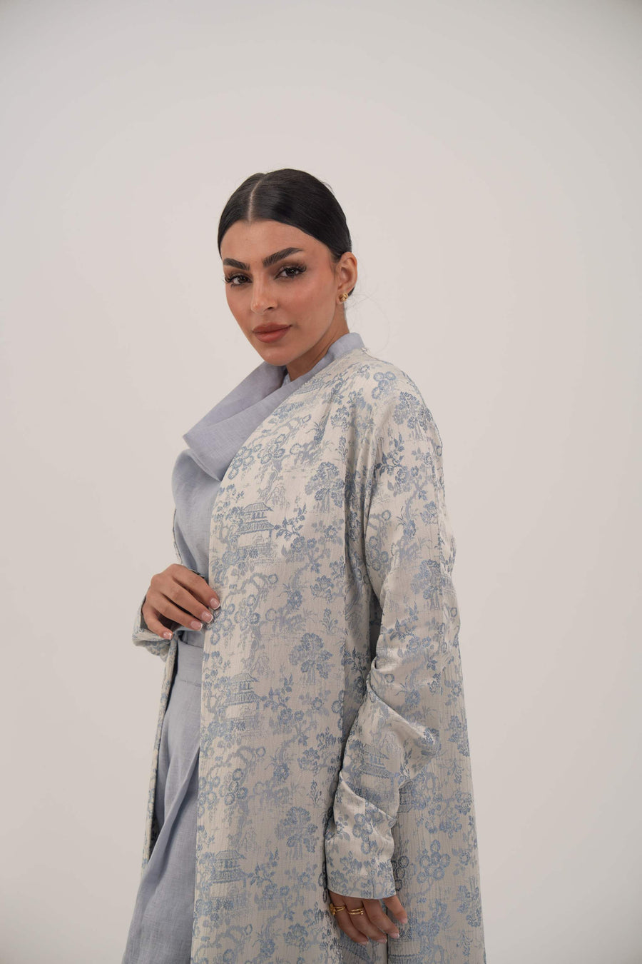 Woman wearing a light blue jacquard silk open-front abaya with a subtle elegant pattern and simple lapel against a plain background.