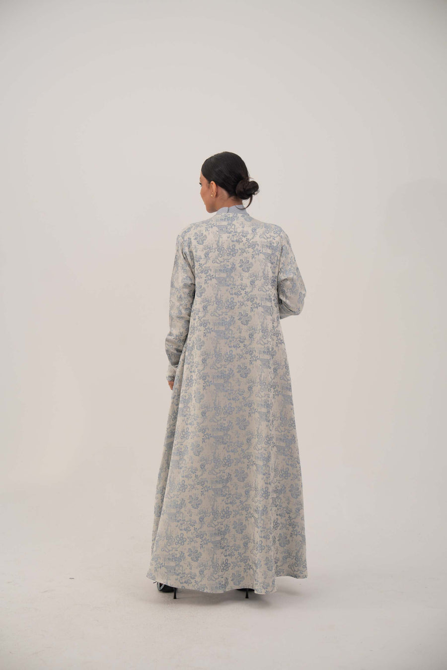 Back view of a woman wearing a long open-front jacquard silk abaya with a soft elegant pattern, simple lapel, and loose sleeves.