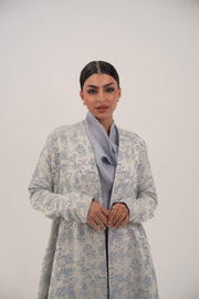 Woman wearing a light blue jacquard silk open-front abaya with a soft floral pattern and simple lapel collar