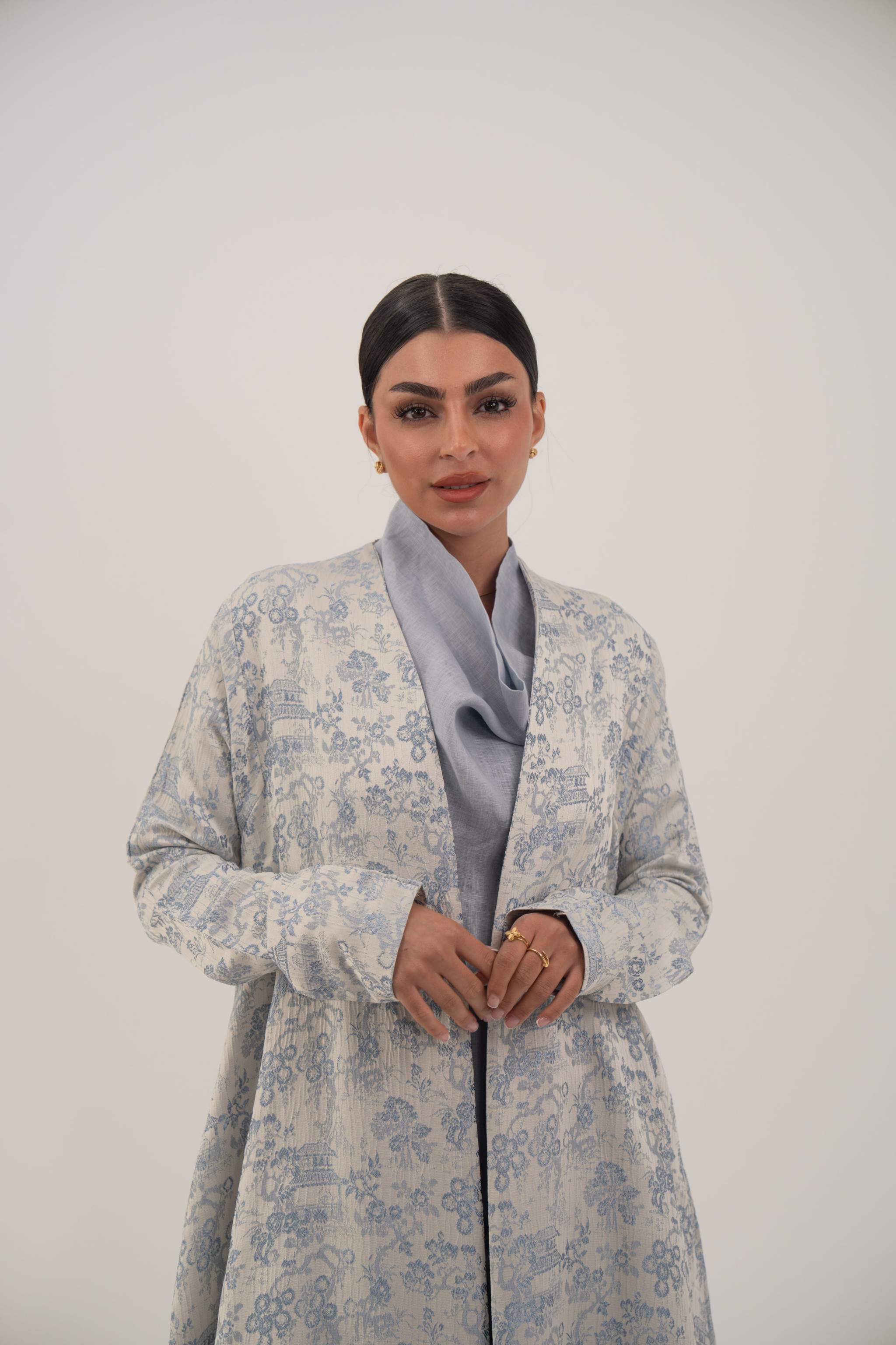 Woman wearing a light blue jacquard silk open-front abaya with a soft floral pattern and simple lapel collar
