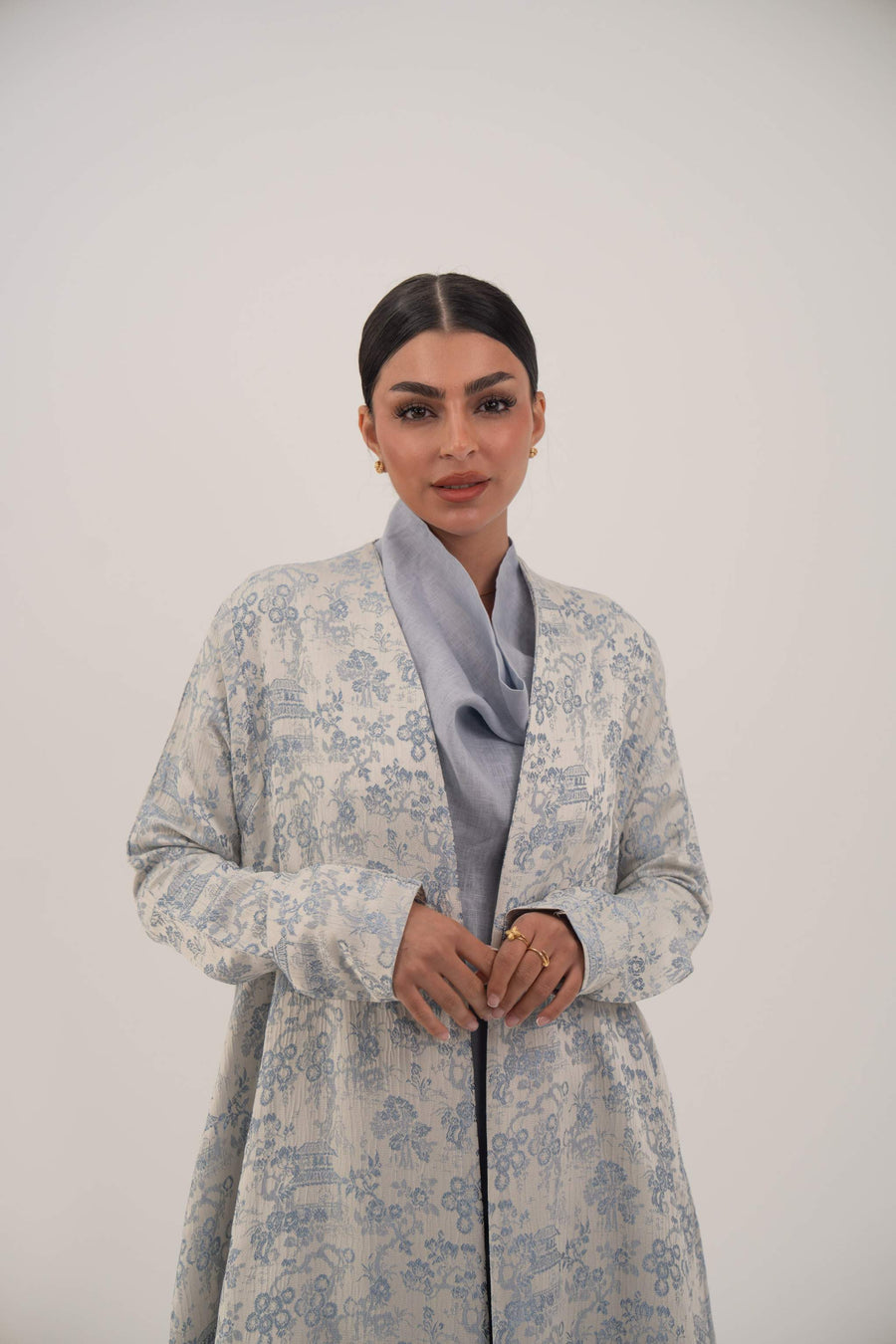 Woman wearing a light blue jacquard silk open-front abaya with a soft floral pattern and simple lapel collar