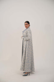Woman wearing an open-front jacquard silk abaya with a soft elegant pattern and simple lapel, standing against a plain background.