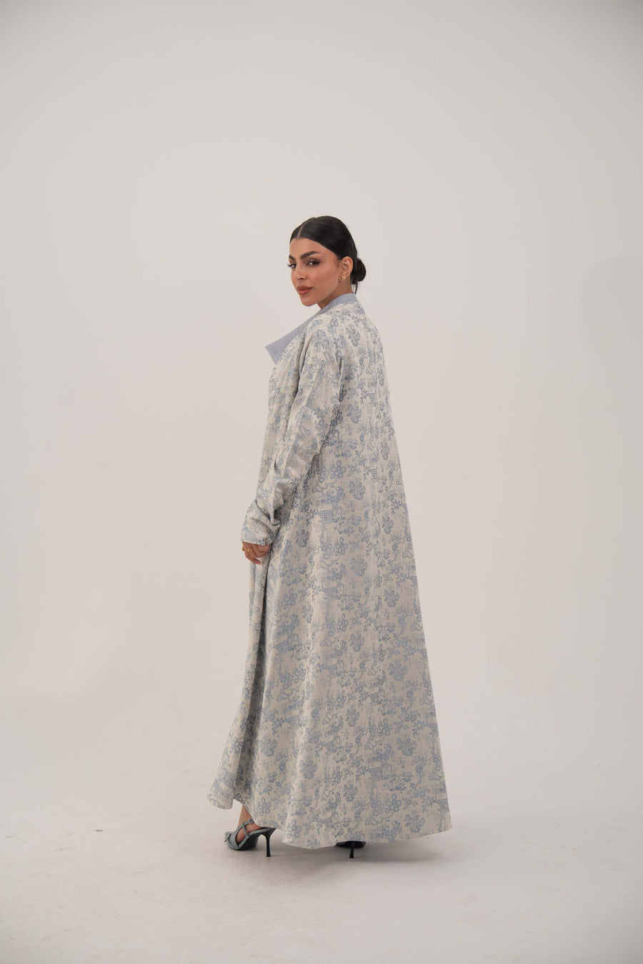 Woman wearing a long, open-front jacquard silk abaya with a soft elegant pattern and simple lapel standing against a plain background