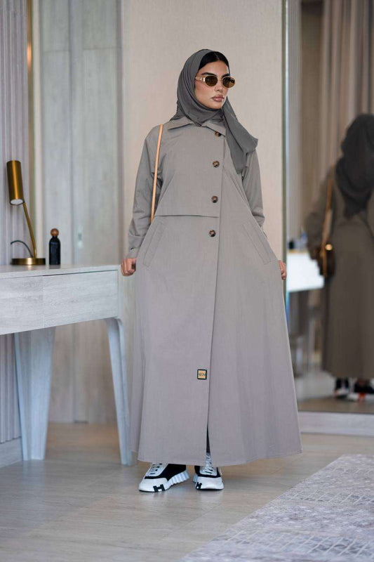 Woman wearing a kaki abaya trenchcoat with buttons and sneakers indoors