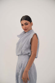 Woman wearing sleeveless light blue linen blouse with draped collar and relaxed fit.