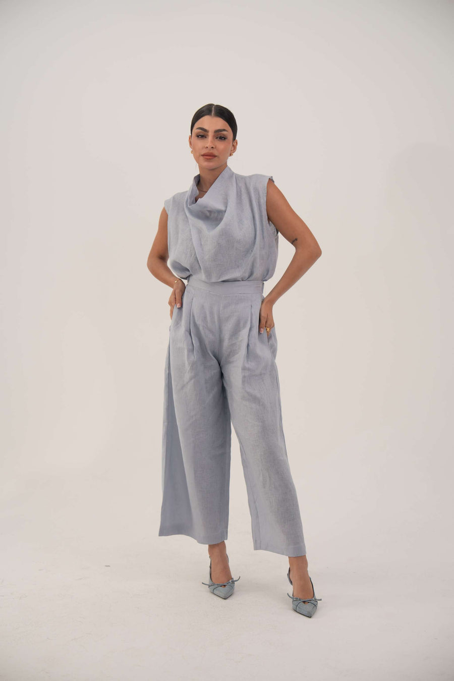 Woman wearing a sleeveless light blue linen blouse with a draped collar and relaxed fit paired with matching wide-leg pants.