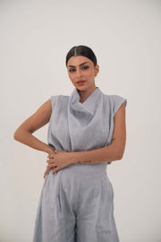 Woman wearing a light blue sleeveless linen blouse with a draped collar and relaxed fit.