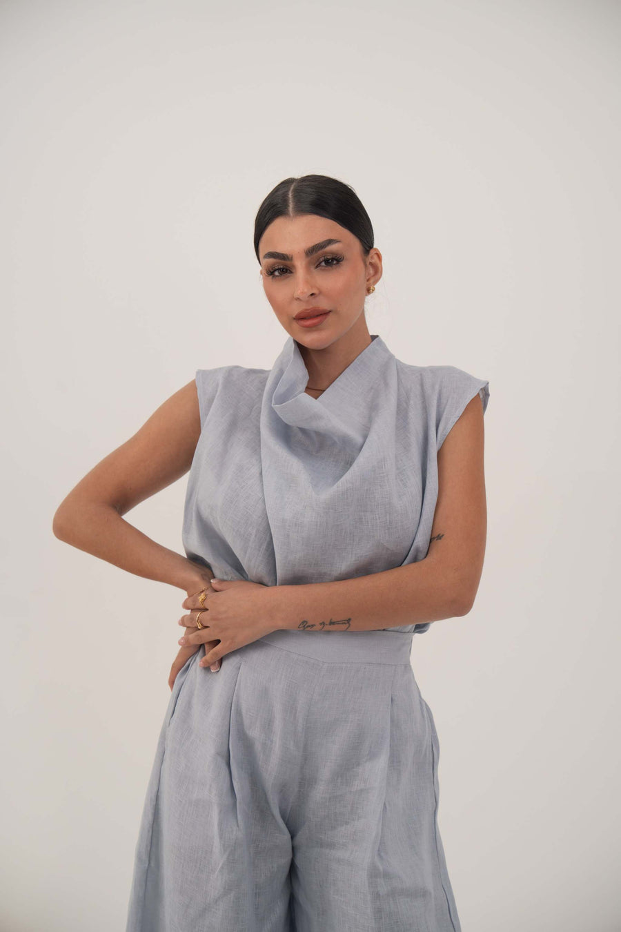 Woman wearing a light blue sleeveless linen blouse with a draped collar and relaxed fit.