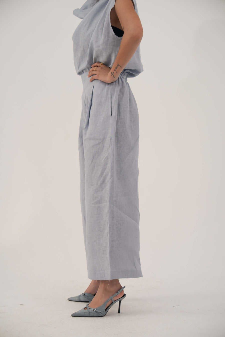 Light blue wide-leg linen pants with high waist and front pleats, cropped above ankle, styled with matching top and heels.