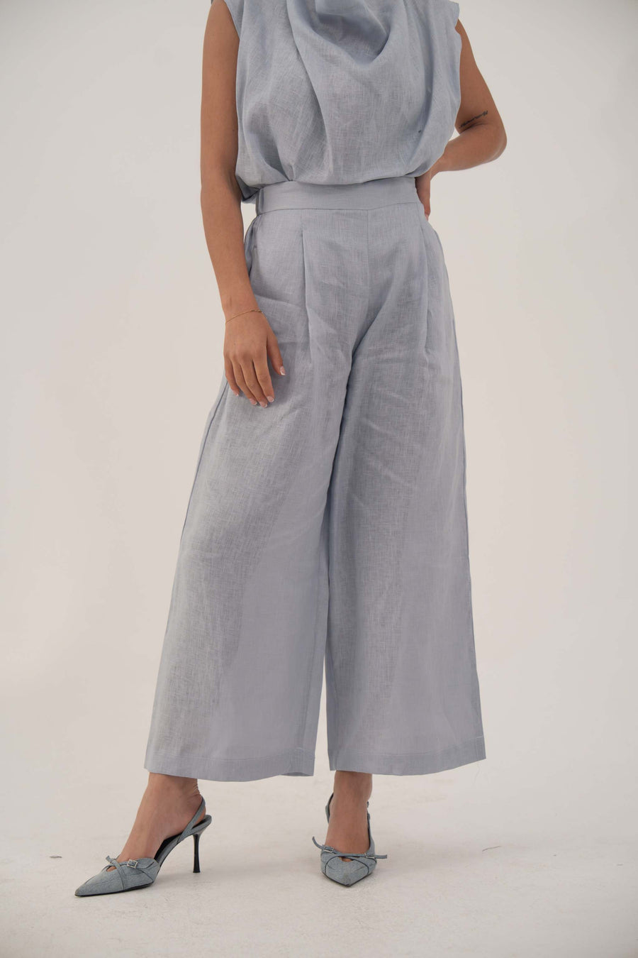 Light blue wide-leg linen pants with high waist and front pleats, cropped above ankle for a modern look