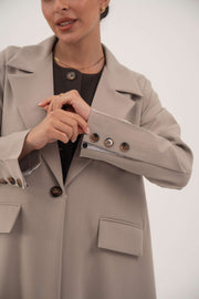 Light taupe beige blazer abaya with notched collar, single front button, brown marbled sleeve buttons, false flap pockets, and A-line cut.