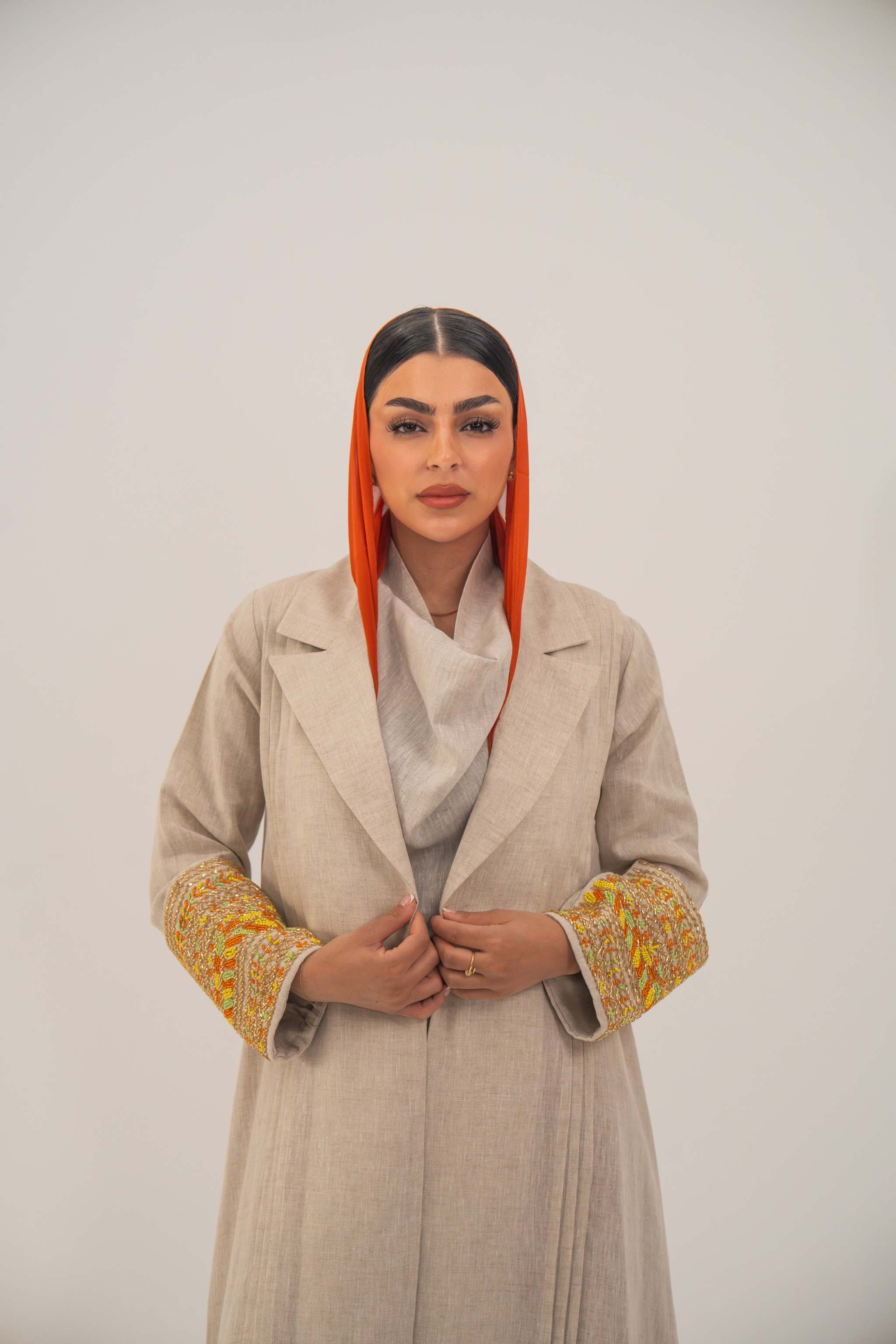 Beige linen blend abaya with blazer-style cut and vibrant orange, gold, and green embroidery on sleeves, paired with an orange headscarf - 