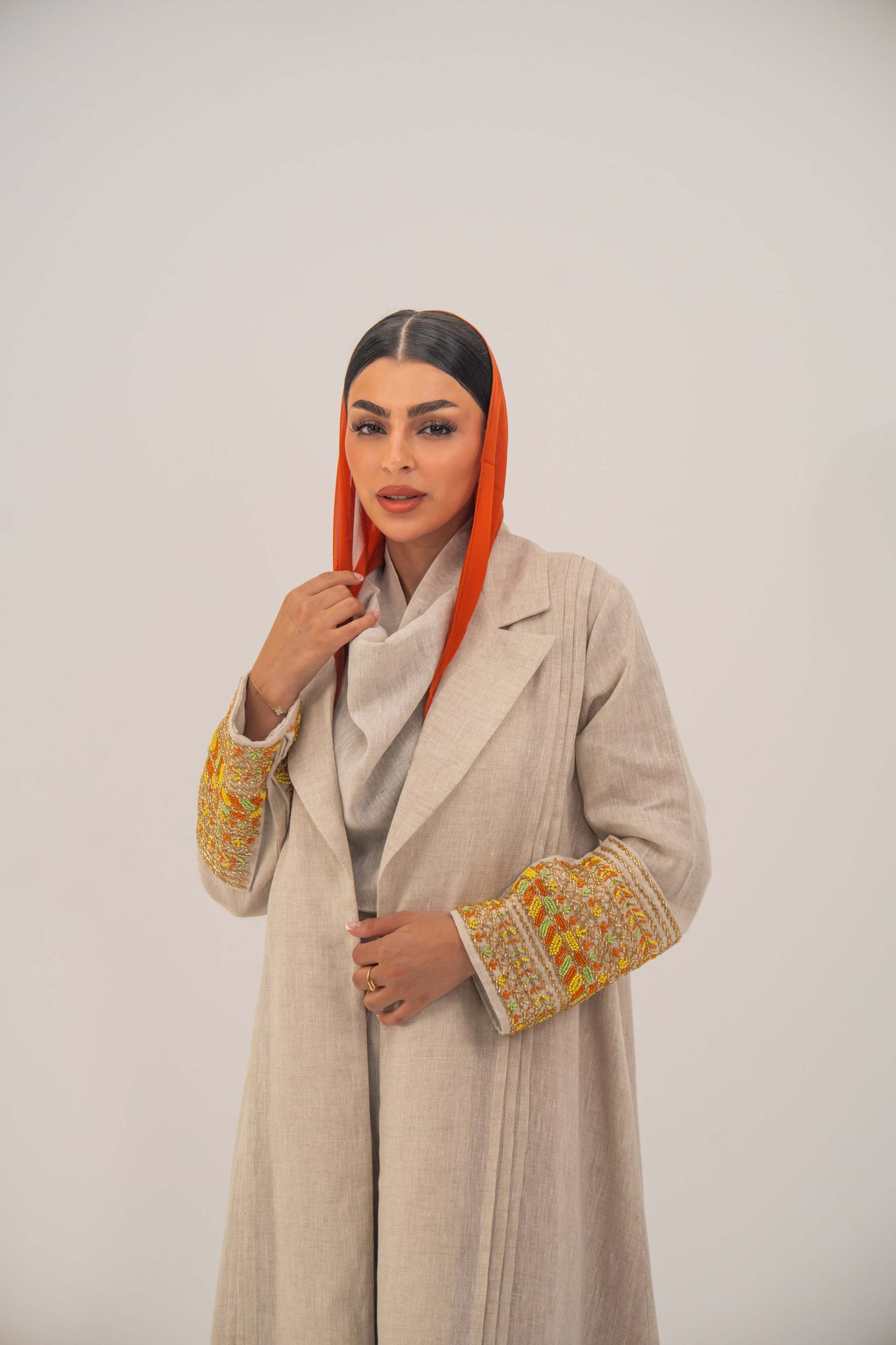Beige linen blend abaya with tailored blazer-style cut, vibrant orange, gold, and green embroidery on sleeves, and subtle orange chiffon lining - sophisticated abaya