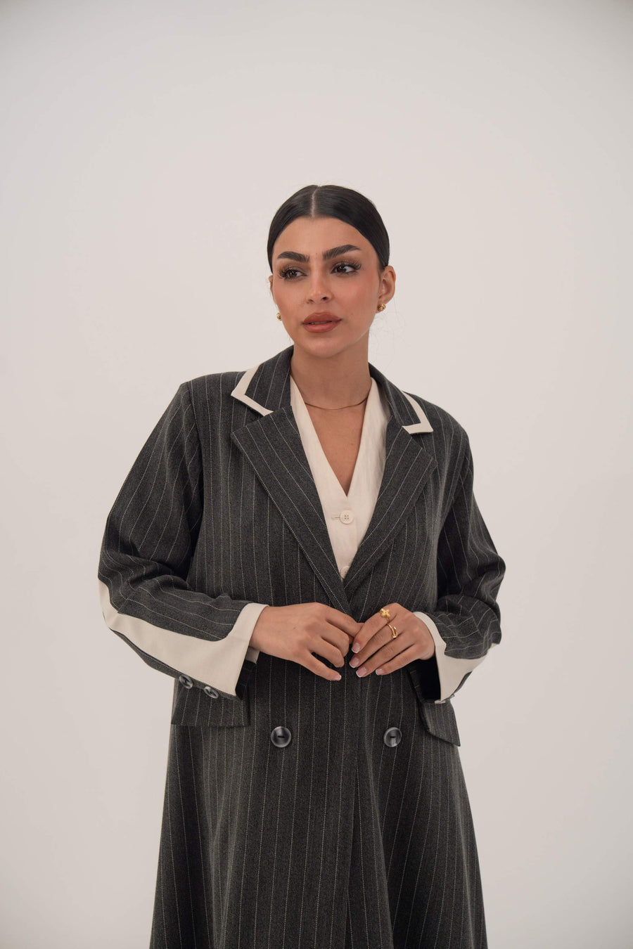 Woman wearing Ashmood elegant black pinstripe double-breasted blazer-style abaya with off-white inner cuffs and sharp lapels