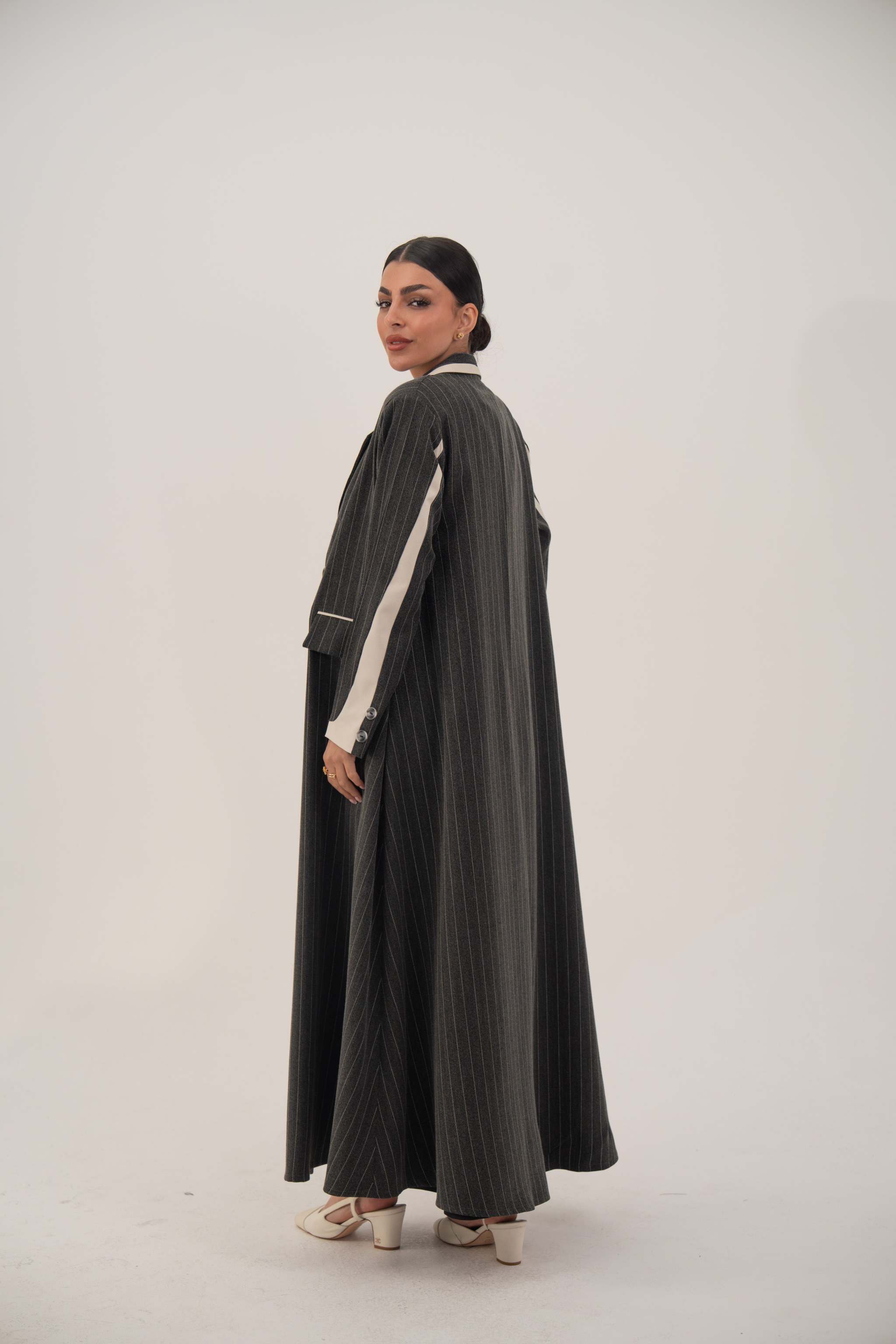 Elegant black blazer-style abaya with white pinstripes, off-white inner cuffs, and full-length hem, worn by a model against a neutral background.