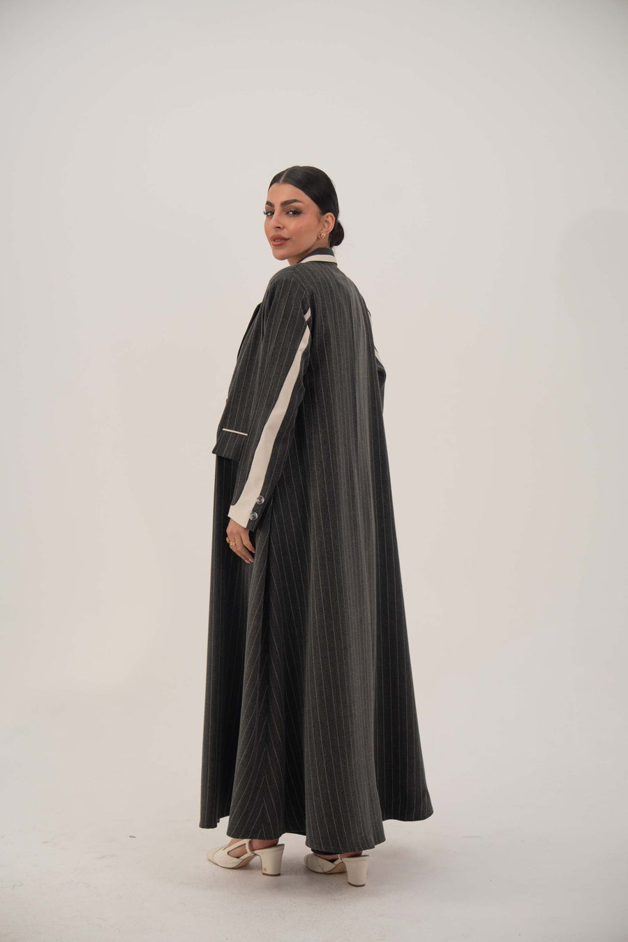 Elegant black blazer-style abaya with white pinstripes, off-white inner cuffs, and full-length hem, worn by a model against a neutral background.