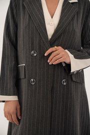 Black double-breasted blazer-style abaya with white pinstripes and off-white inner cuffs, featuring sharp lapels and faux pockets.