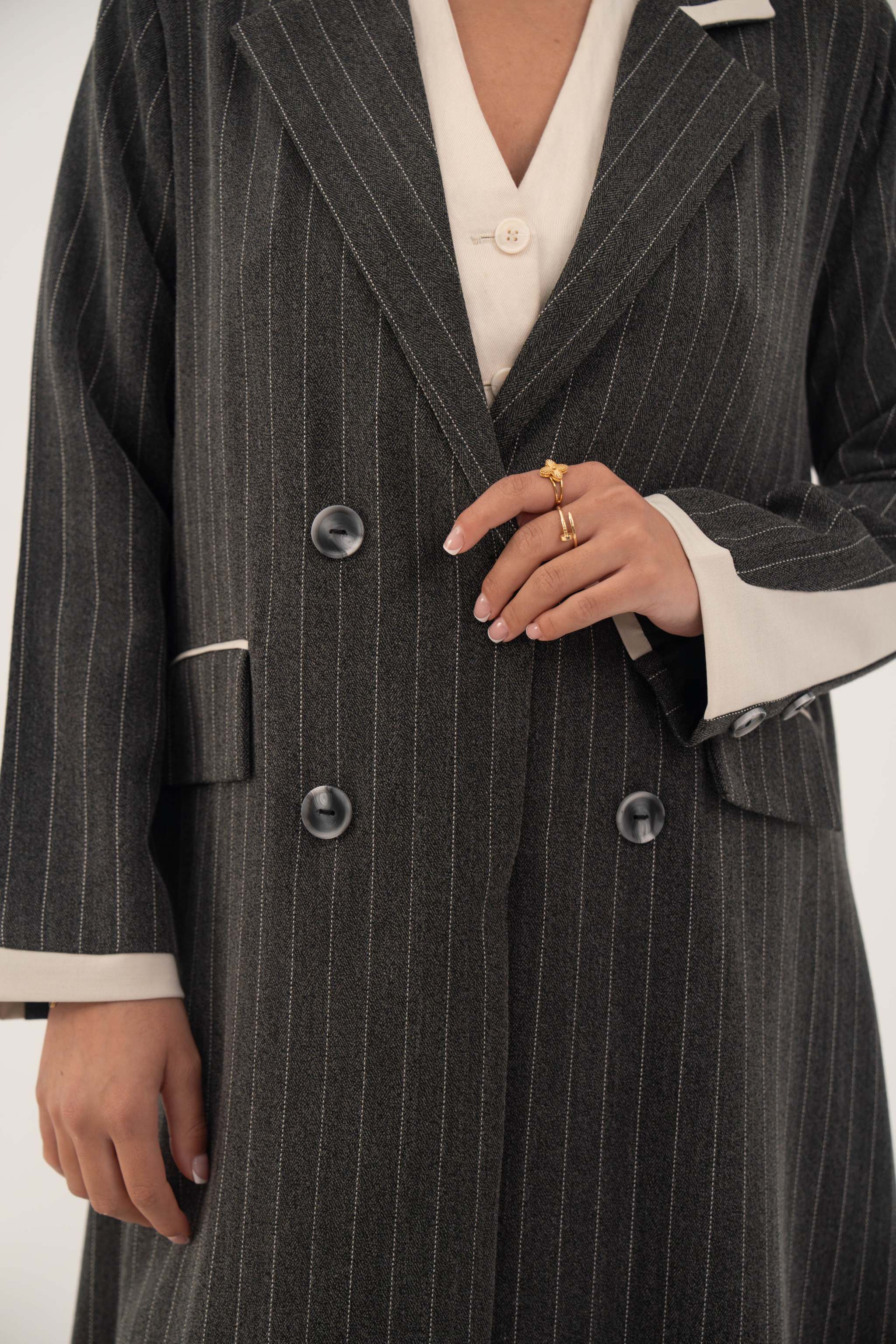Black double-breasted blazer-style abaya with white pinstripes and off-white inner cuffs, featuring sharp lapels and faux pockets.