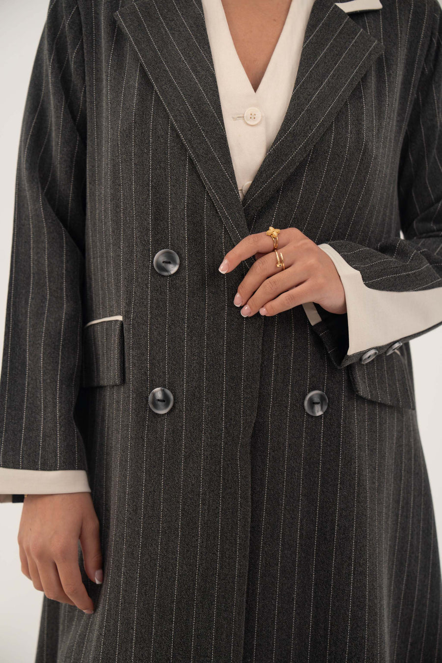Black double-breasted blazer-style abaya with white pinstripes and off-white inner cuffs, featuring sharp lapels and faux pockets.