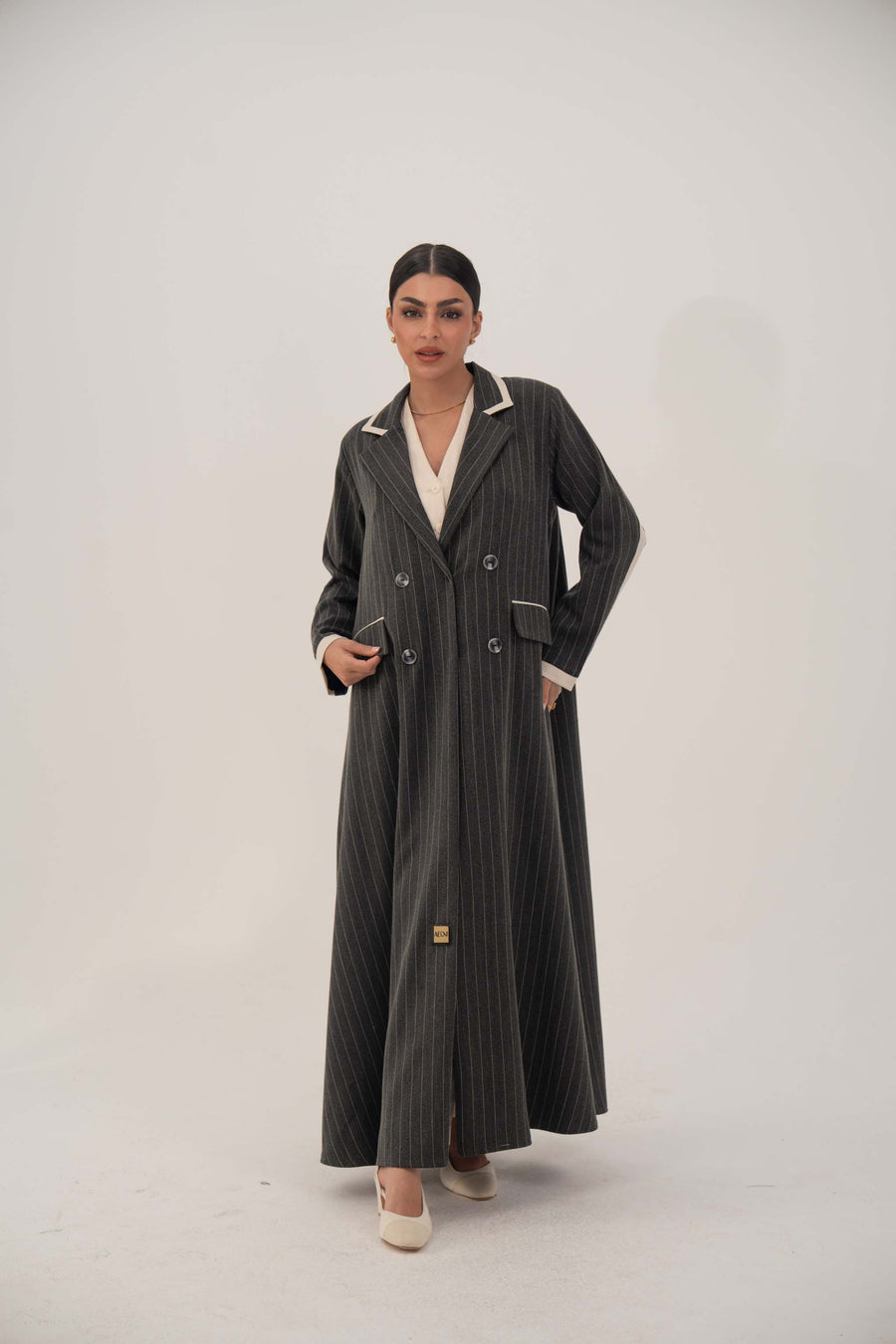 Woman wearing elegant black pinstriped blazer-style abaya with white lapels and cuffs, double-breasted design, and full-length hem.