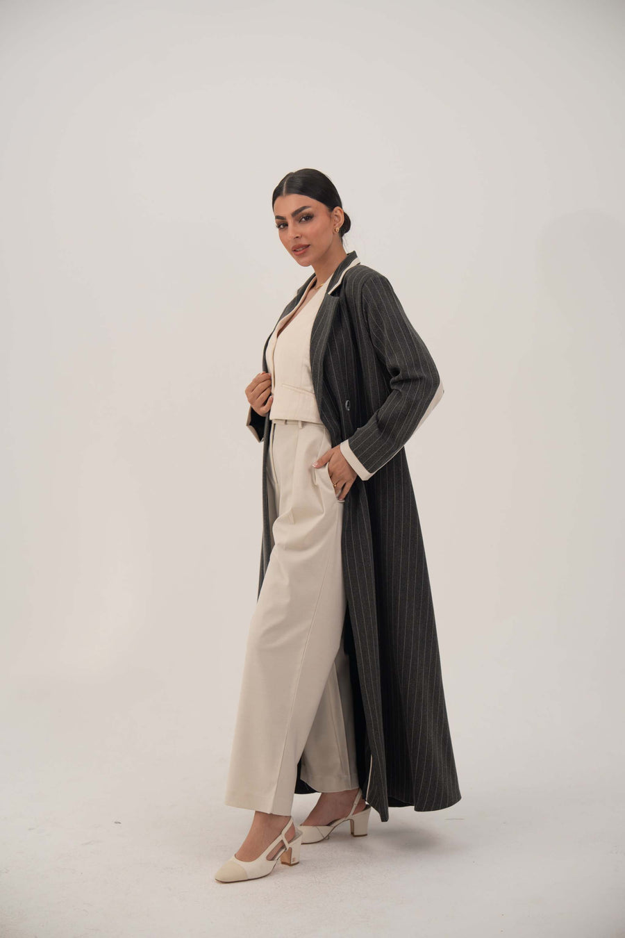 Elegant black pinstriped blazer-style abaya with off-white inner cuffs and double-breasted design on a woman wearing beige outfit and heels