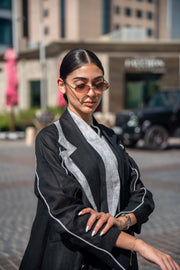 Woman wearing a black blazer abaya with white piping and sharp lapels in an urban setting
