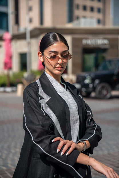 Woman wearing a black blazer abaya with white piping and sharp lapels in an urban setting