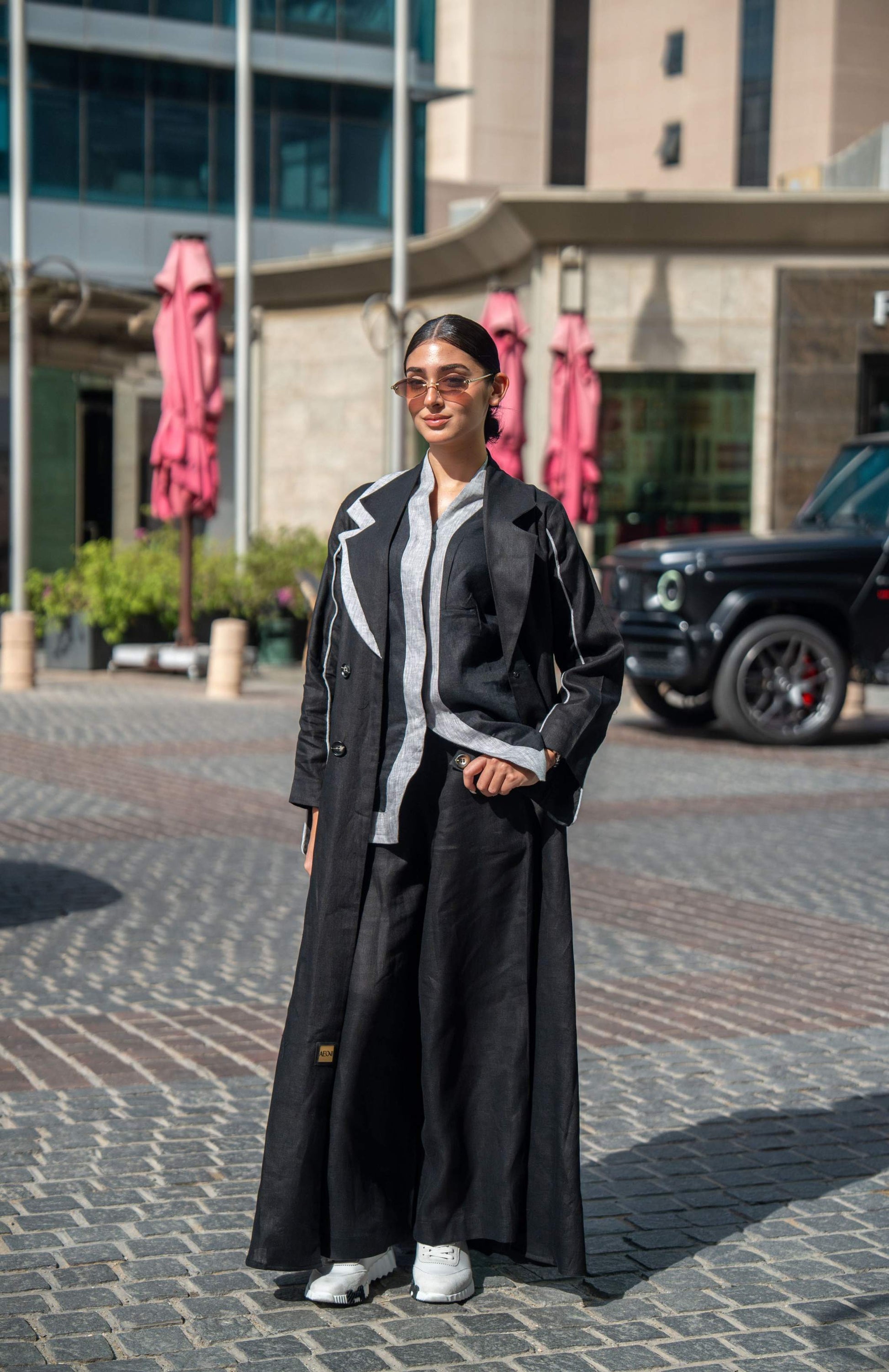 Woman wearing black blazer abaya with sharp lapels and white piping, styled for modern street and professional look.