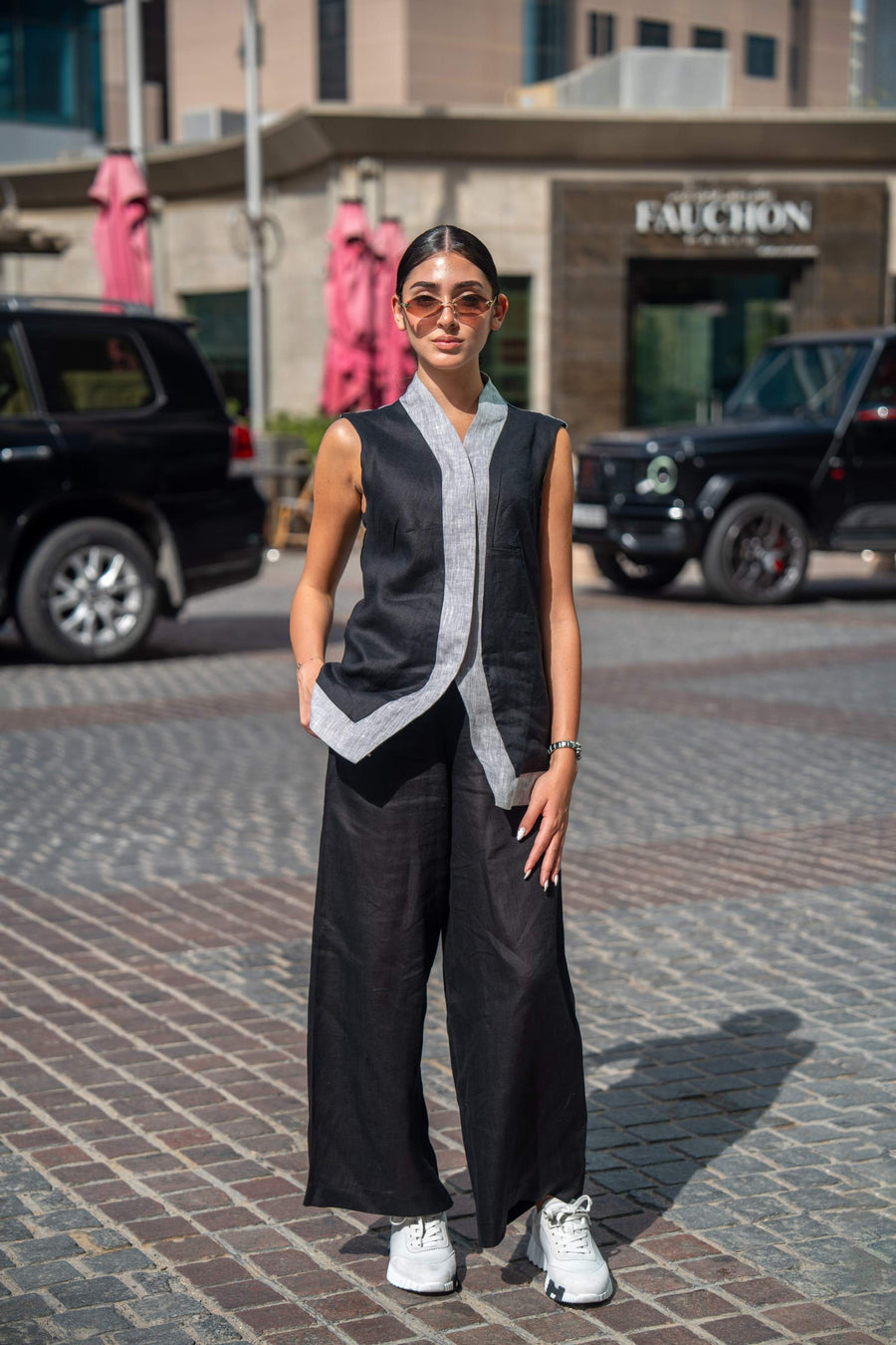 Woman wearing a black and gray sleeveless mist vest with wide-leg pants and white sneakers standing on a cobblestone street.