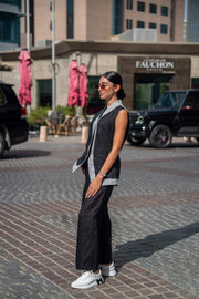 Woman wearing black mist vest and wide-leg pants with sunglasses walking outdoors on cobblestone street