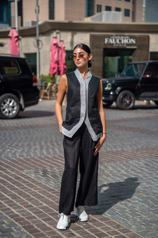 Woman wearing black Mist Pant with sleeveless top and white sneakers standing outdoors on a cobblestone street