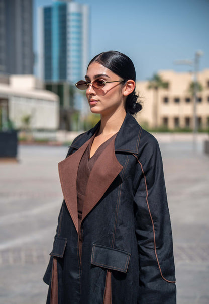 Woman wearing a modern black and brown linen Velora abaya with wide lapels and clean lines in an urban setting
