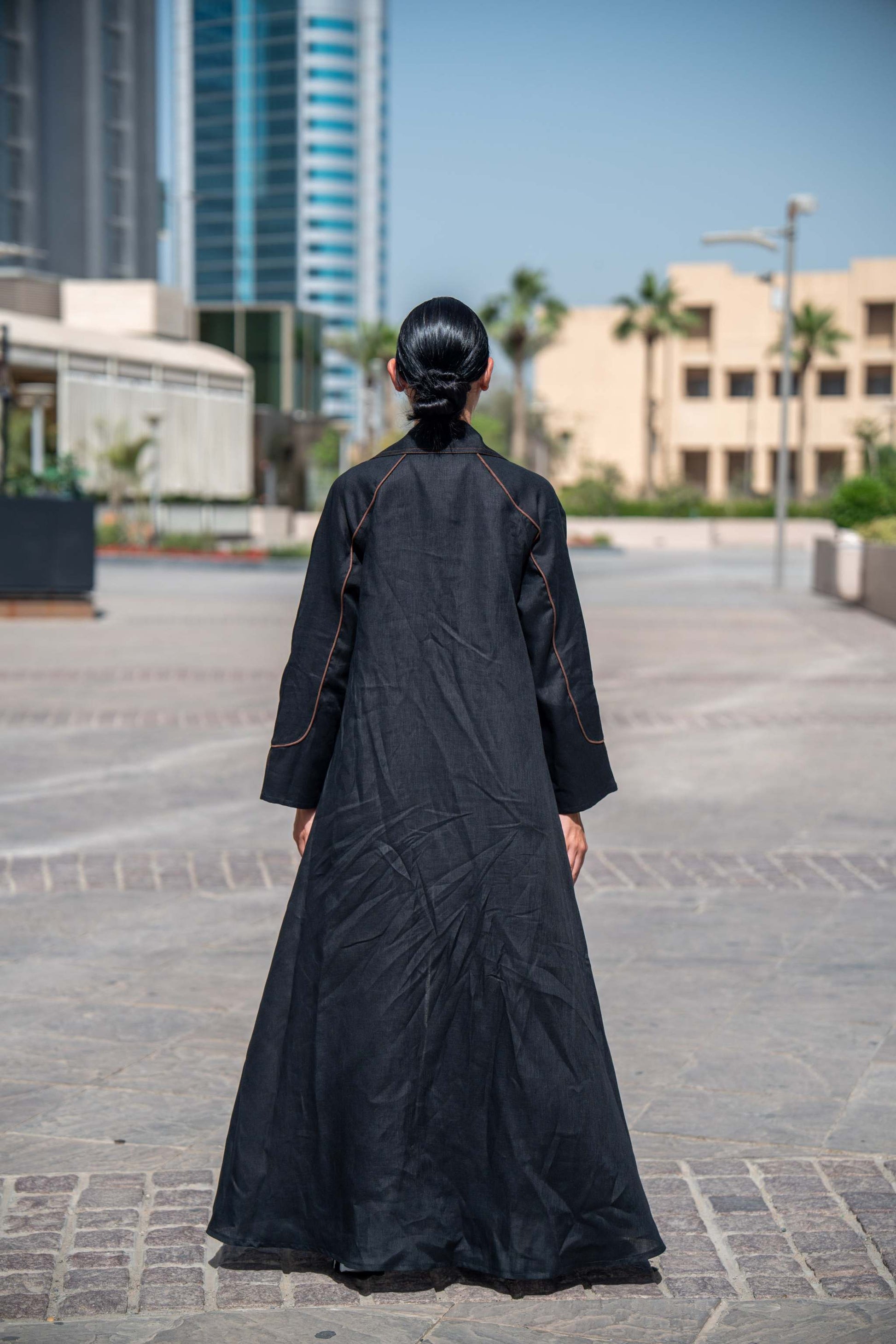 Back view of a woman wearing a black and brown linen Velora abaya with wide lapels and clean lines in an urban setting