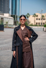 Woman wearing a contemporary abaya in black and brown linen with wide lapels and clean lines, standing outdoors in an urban setting.