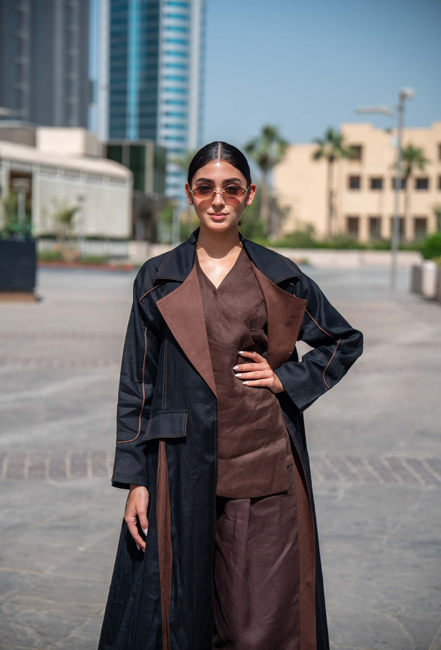 Woman wearing a contemporary abaya in black and brown linen with wide lapels and clean lines, standing outdoors in an urban setting.