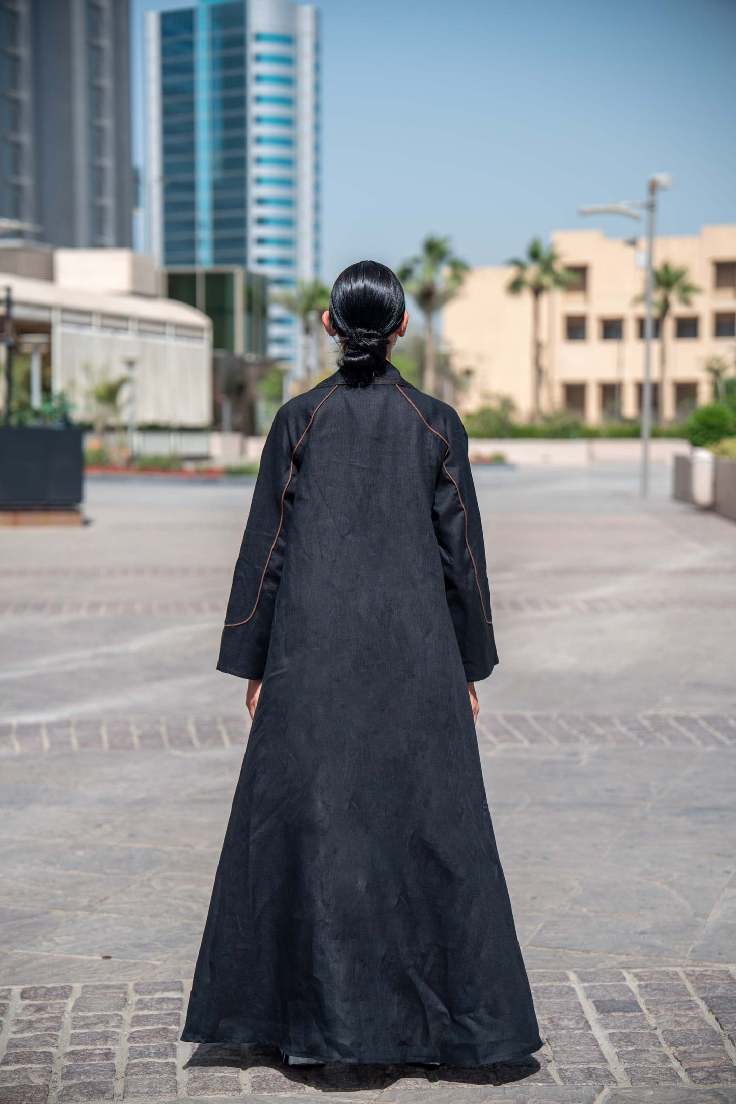 Back view of woman wearing modern black Velora abaya with brown linen details and wide lapels in urban setting